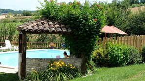 Un espace piscine agrémenté d’une structure en pierre, d’une clôture en bois et d’une pergola surmontée d’un parasol rouge.