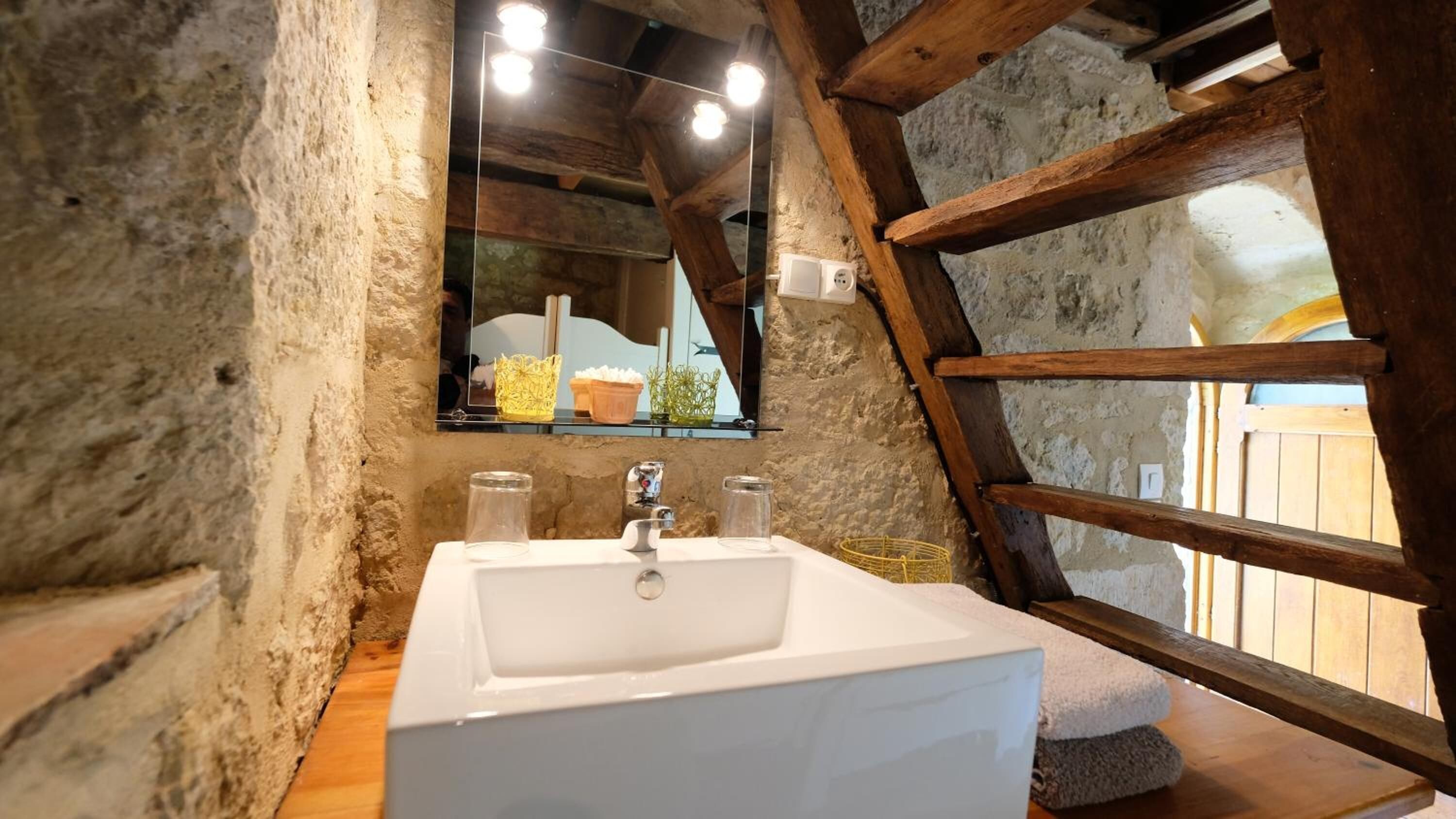 Un bagno rustico con un lavandino bianco, travi in legno e un'ampia finestra.