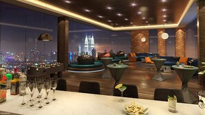 Eine moderne Bar mit Stadtblick, Sitzgelegenheiten und einer Theke mit Gläsern und Flaschen.