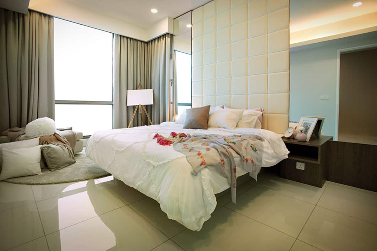 A modern hotel room with a large bed, a bedside table, a nightstand, a lamp, and a view of the outside.