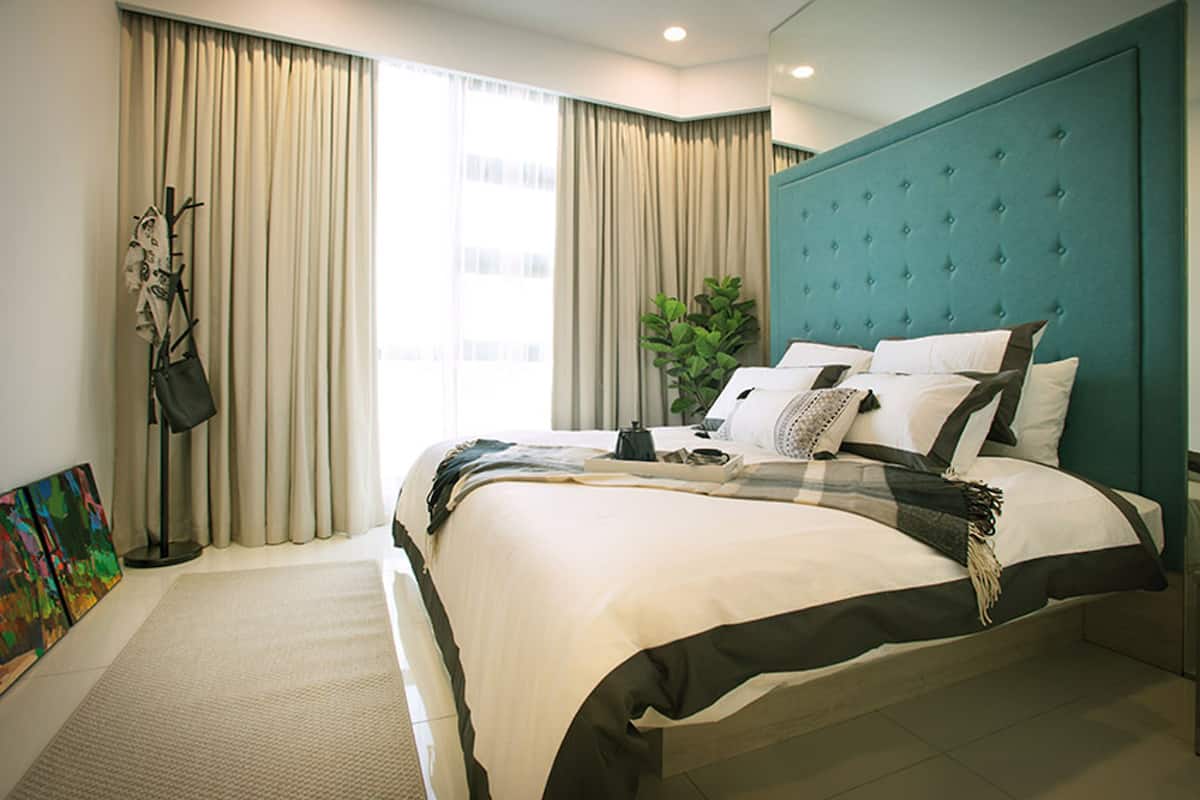 A hotel room with a large bed, a teal headboard, and a view of the city through the window.