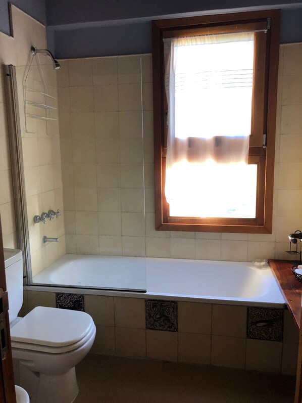 Un baño con bañera, inodoro y una ventana con cortinas.
