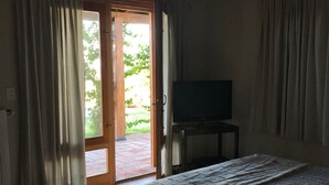 A bedroom with a bed, a television on a stand, and a door leading to an outdoor area.