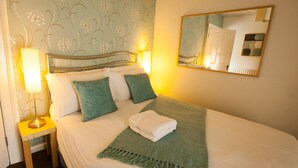 A neatly made bed with a green throw blanket and pillows, a bedside lamp, and a mirror on the wall. - Holly Bush Inn (Hexham)