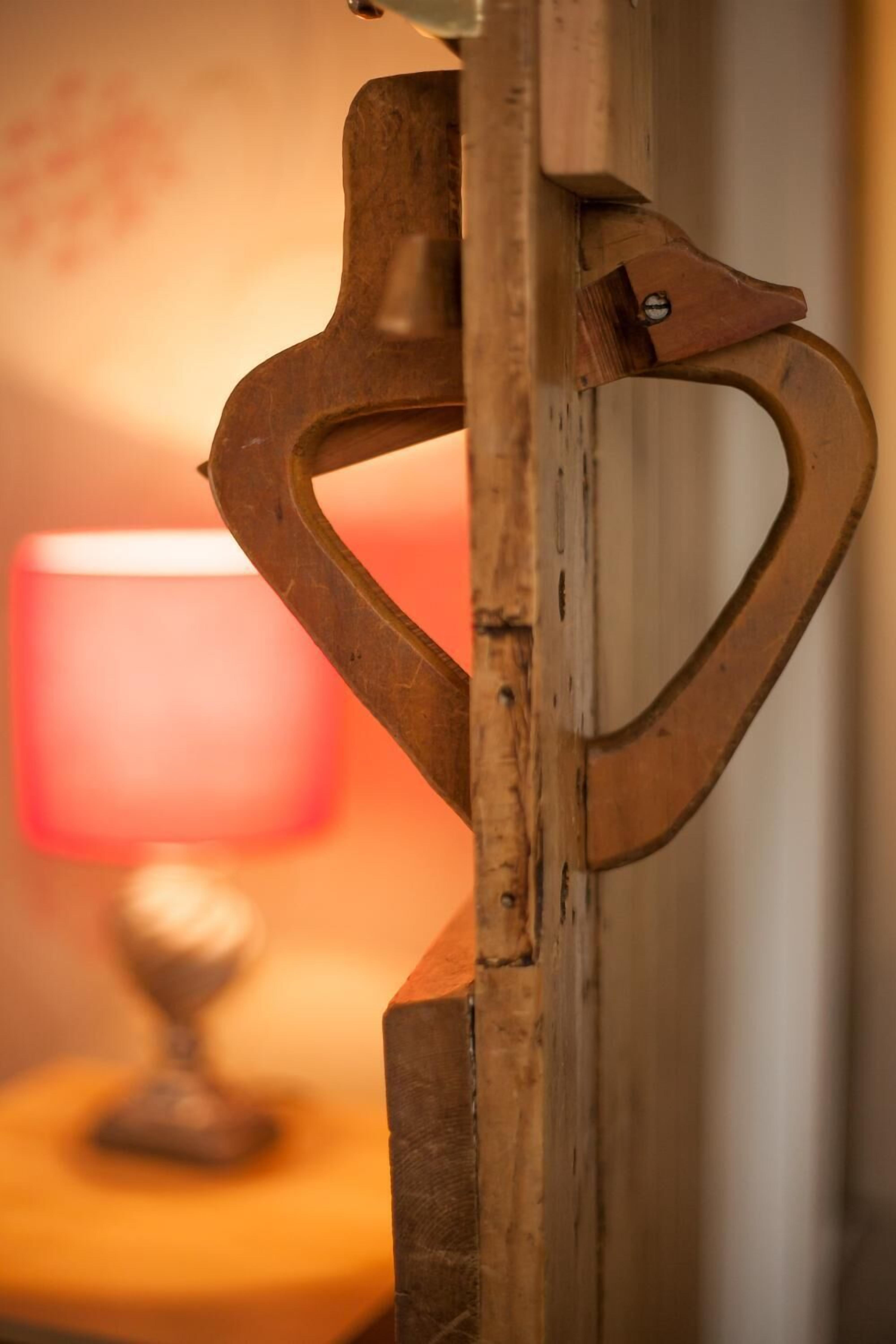 A wooden object with a heart-shaped cutout, possibly a decorative piece or part of furniture, with a blurred background featuring a lamp and a spherical object on a surface.