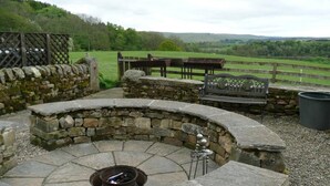 A stone-built outdoor seating area with a circular fire pit, stone walls, and a bench. - Holly Bush Inn (Hexham)