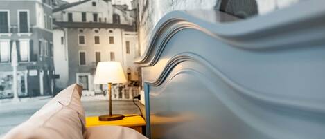 A bed with a pillow, a lamp, and a view of buildings through a window.