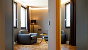Una habitación de hotel moderna con piso de madera en patrón de espiga, dos sofás grises, una mesita redonda y una lámpara de pie.