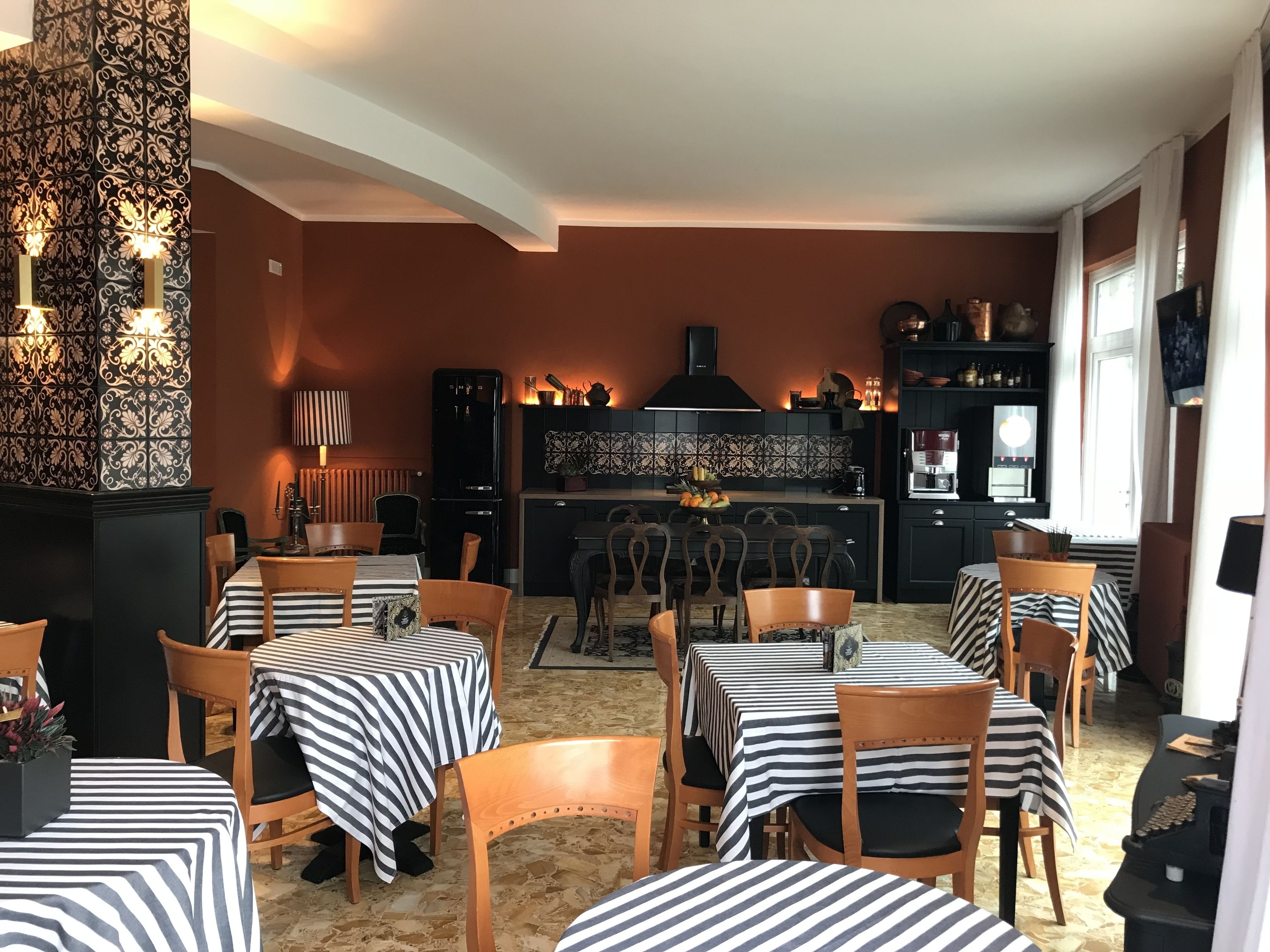Un comedor con manteles a rayas y sillas de madera, una cocina con armarios negros, y una pared decorativa con baldosas estampadas.