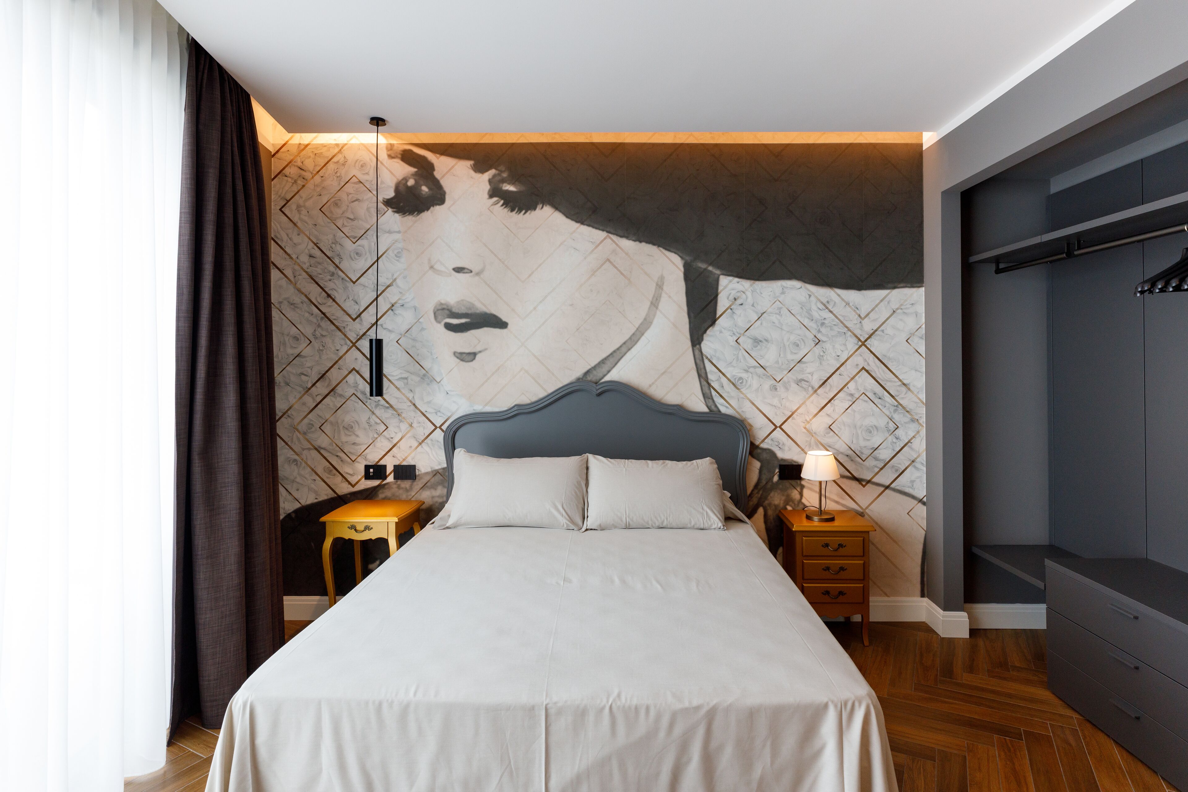 A modern bedroom with a large bed, a headboard, a nightstand, a lamp, and a wardrobe.