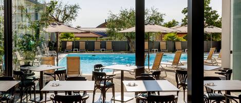 A poolside area with tables and chairs, a swimming pool, and umbrellas.