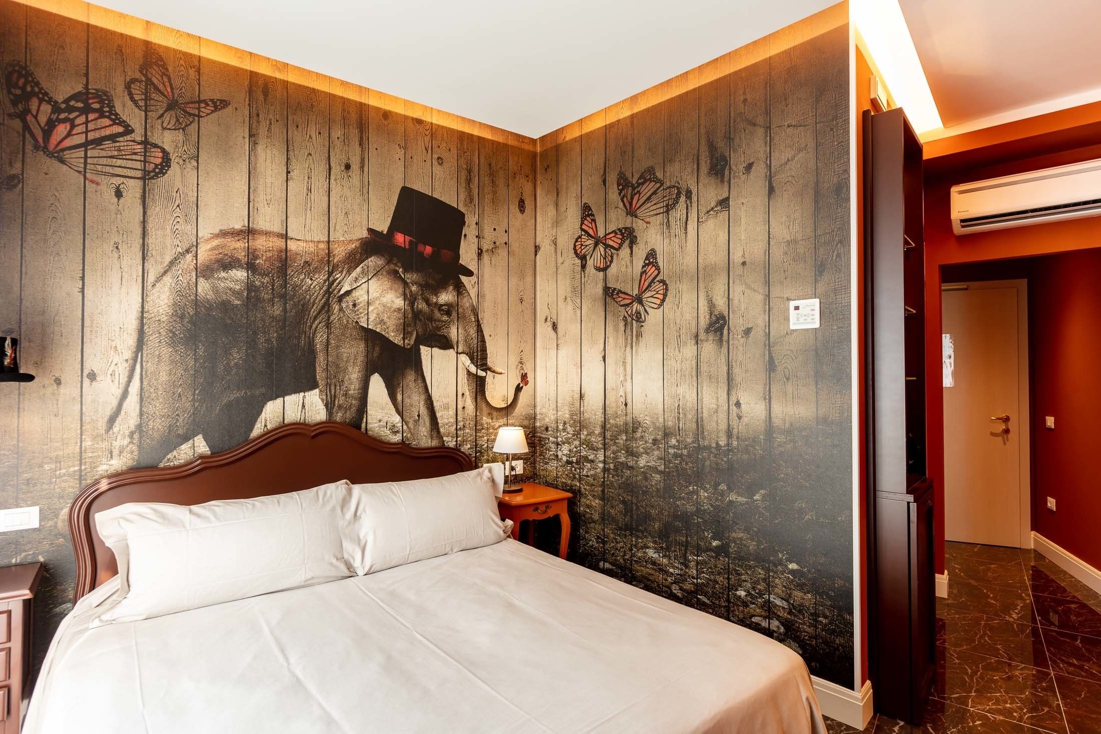 Una habitación de hotel con cama, mesita de noche, un mural en la pared y una puerta.