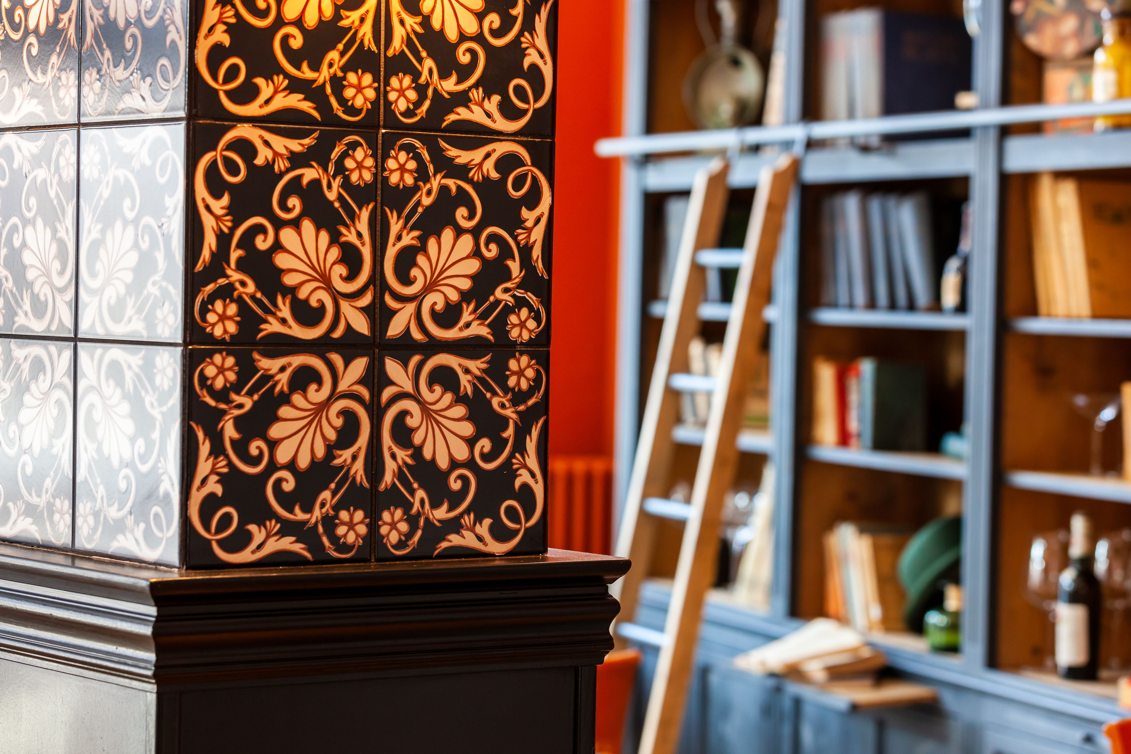 Une partie d’un bâtiment ornée de carreaux noirs et orange, avec une bibliothèque en bois et une échelle appuyée contre.