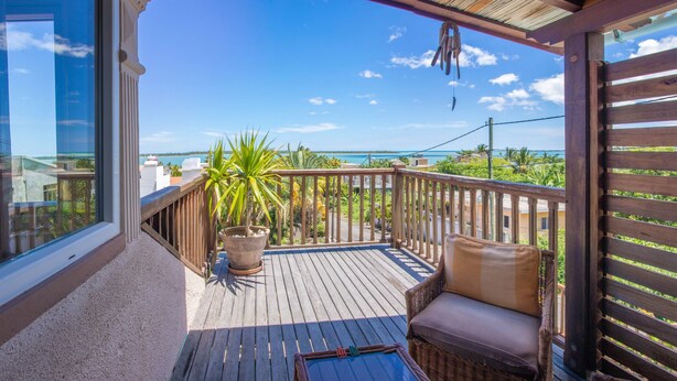 A wooden deck with a wicker sofa and a potted plant. - Blue Lagoon Villa (La Gaulette)