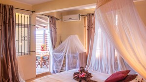 A bedroom with a canopy bed, a wooden floor, and a view of the outside. - Blue Lagoon Villa (La Gaulette)