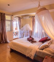 A bedroom with a canopy bed, a wooden floor, and a view of the outside.