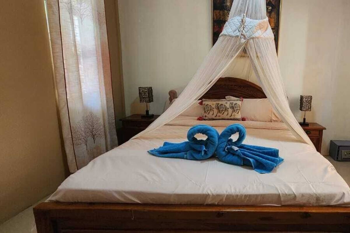 Una cama bien arreglada con dosel, dos mesitas de noche con lámparas y un aire acondicionado de pared.