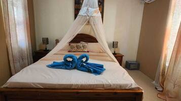 A neatly made bed with a canopy, two bedside tables with lamps, and a wall-mounted air conditioner.
