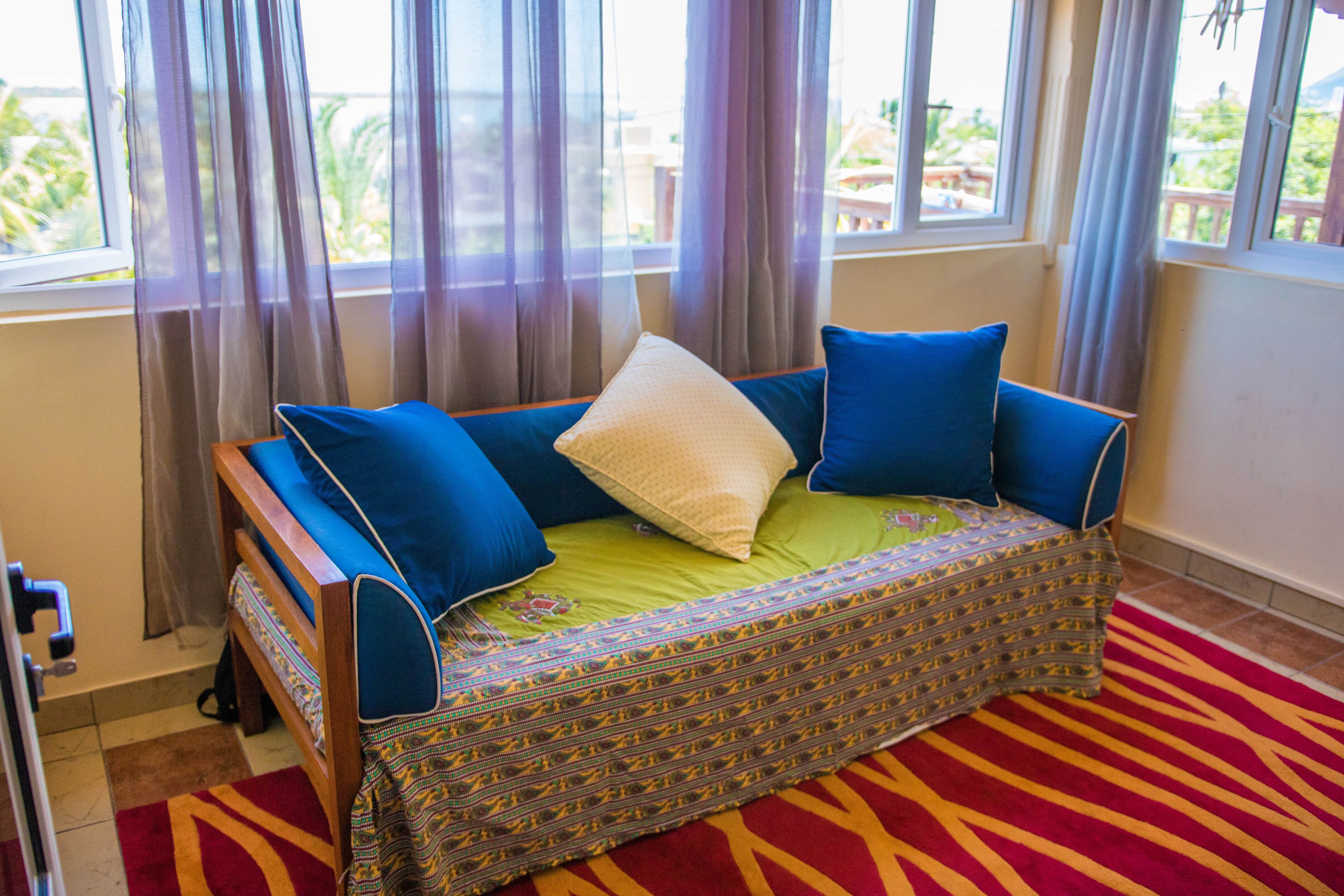 Una habitación con sofá cama, manta estampada y alfombra roja.
