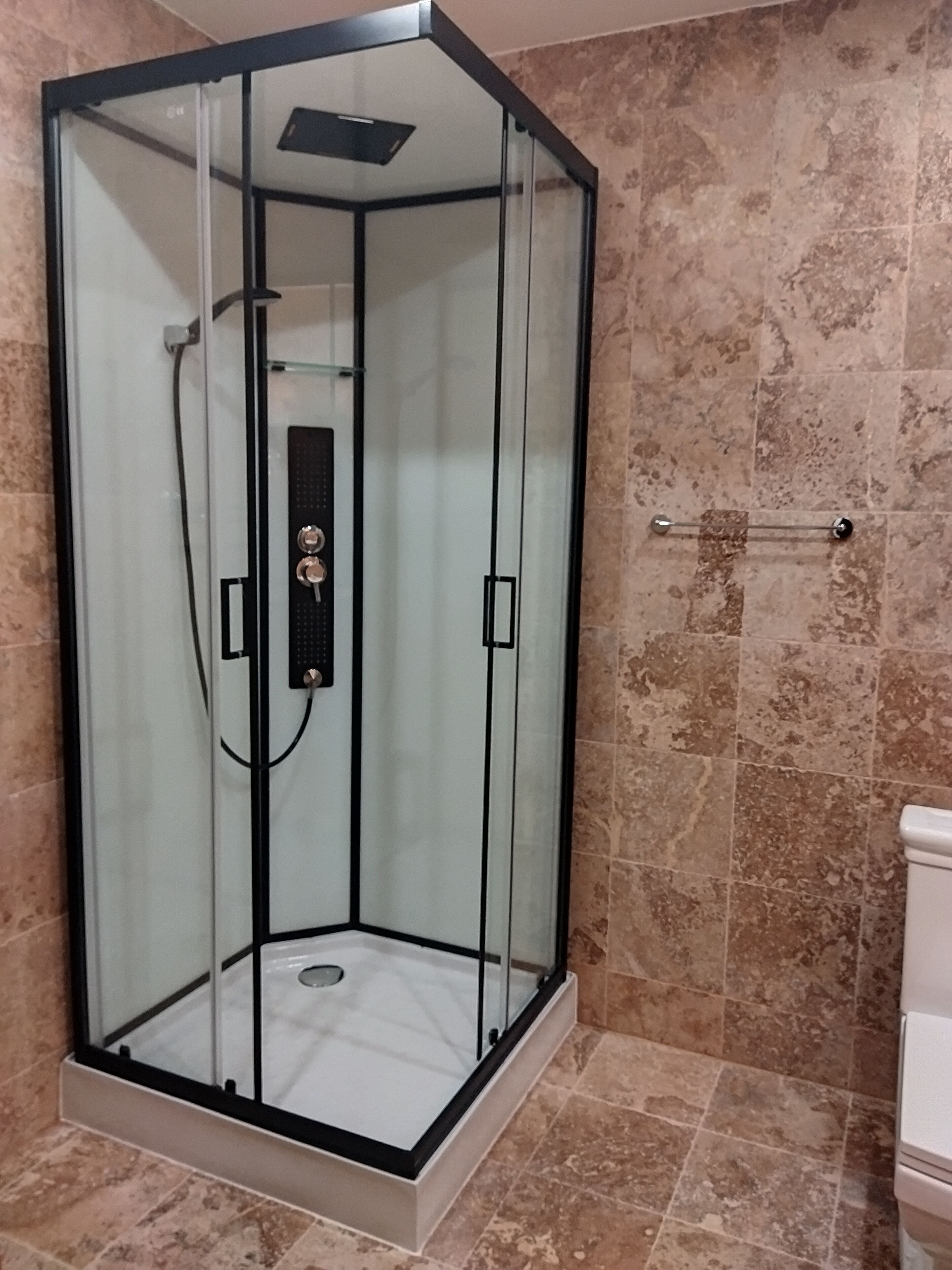 Une cabine de douche fermée par des parois en verre, dotée d’un panneau de commande, d’une barre d’appui et d’un sol carrelé.
