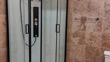 Une cabine de douche fermée par des parois en verre, dotée d’un panneau de commande, d’une barre d’appui et d’un sol carrelé.