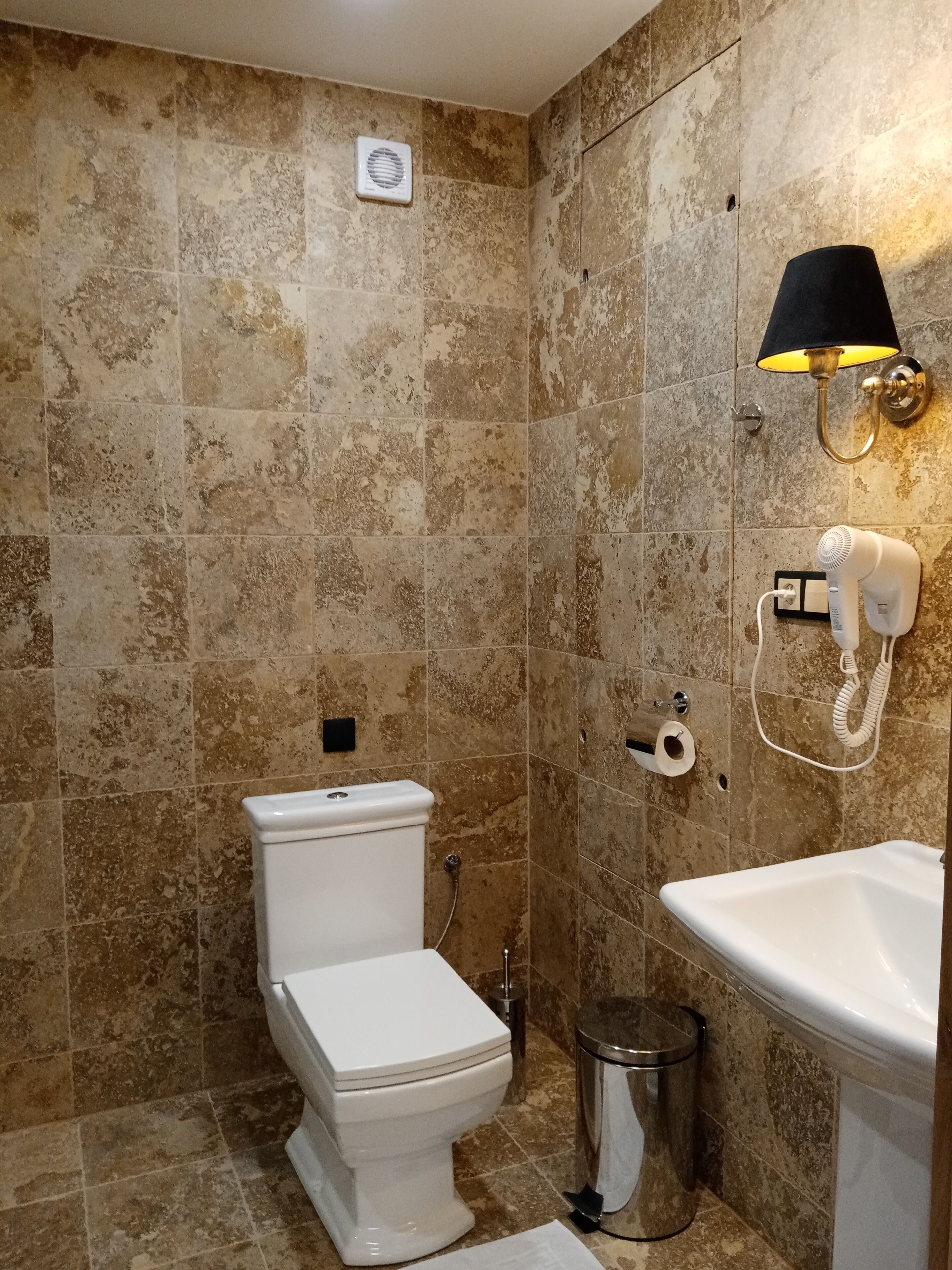A bathroom with a toilet, a sink, a trash bin, and a wall-mounted phone.