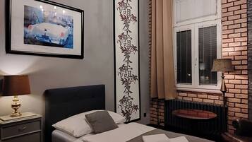 A neatly arranged hotel room with a bed, a bedside lamp, a framed picture on the wall, a window with blinds, and a radiator.