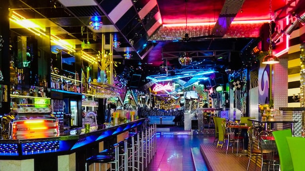 Uma área de bar com um balcão comprido, banquetas e diversas garrafas e copos.