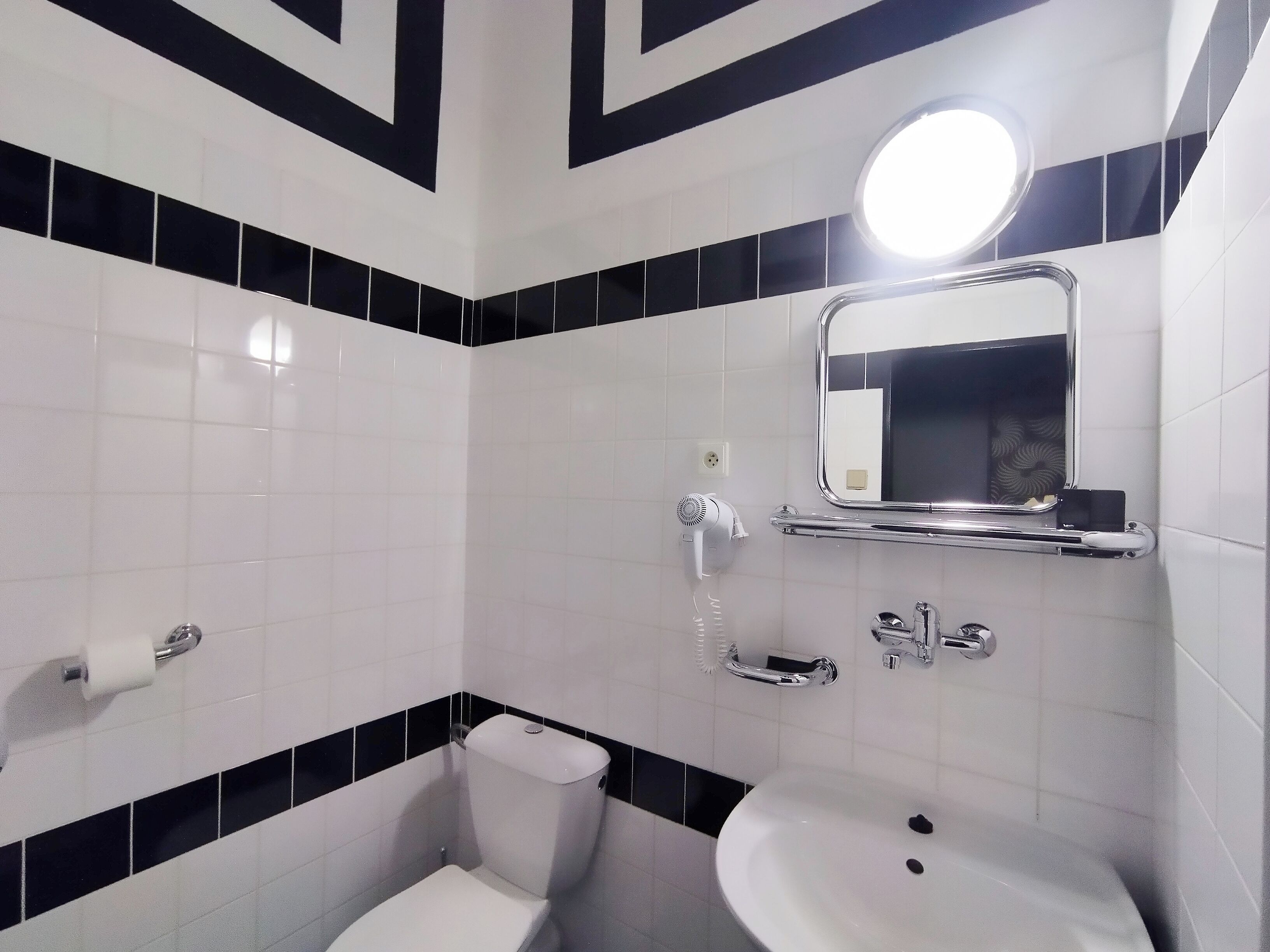 A bathroom with a toilet, sink, and mirror. There is a hairdryer and a soap dish on the wall.