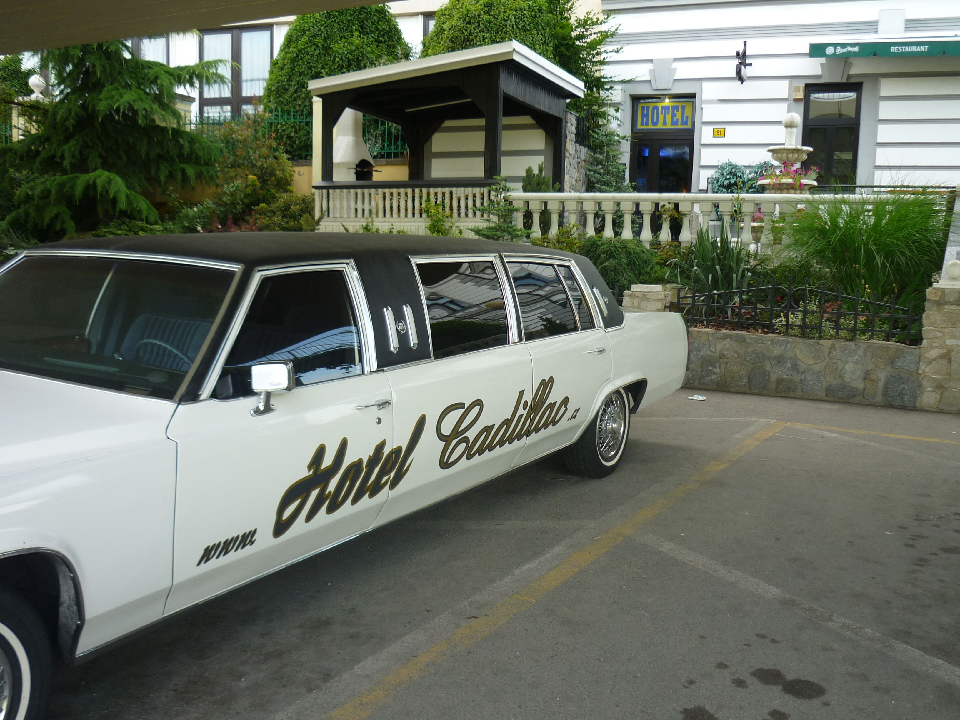 Een klassieke Cadillac auto geparkeerd voor een gebouw met een restaurant en een fontein.