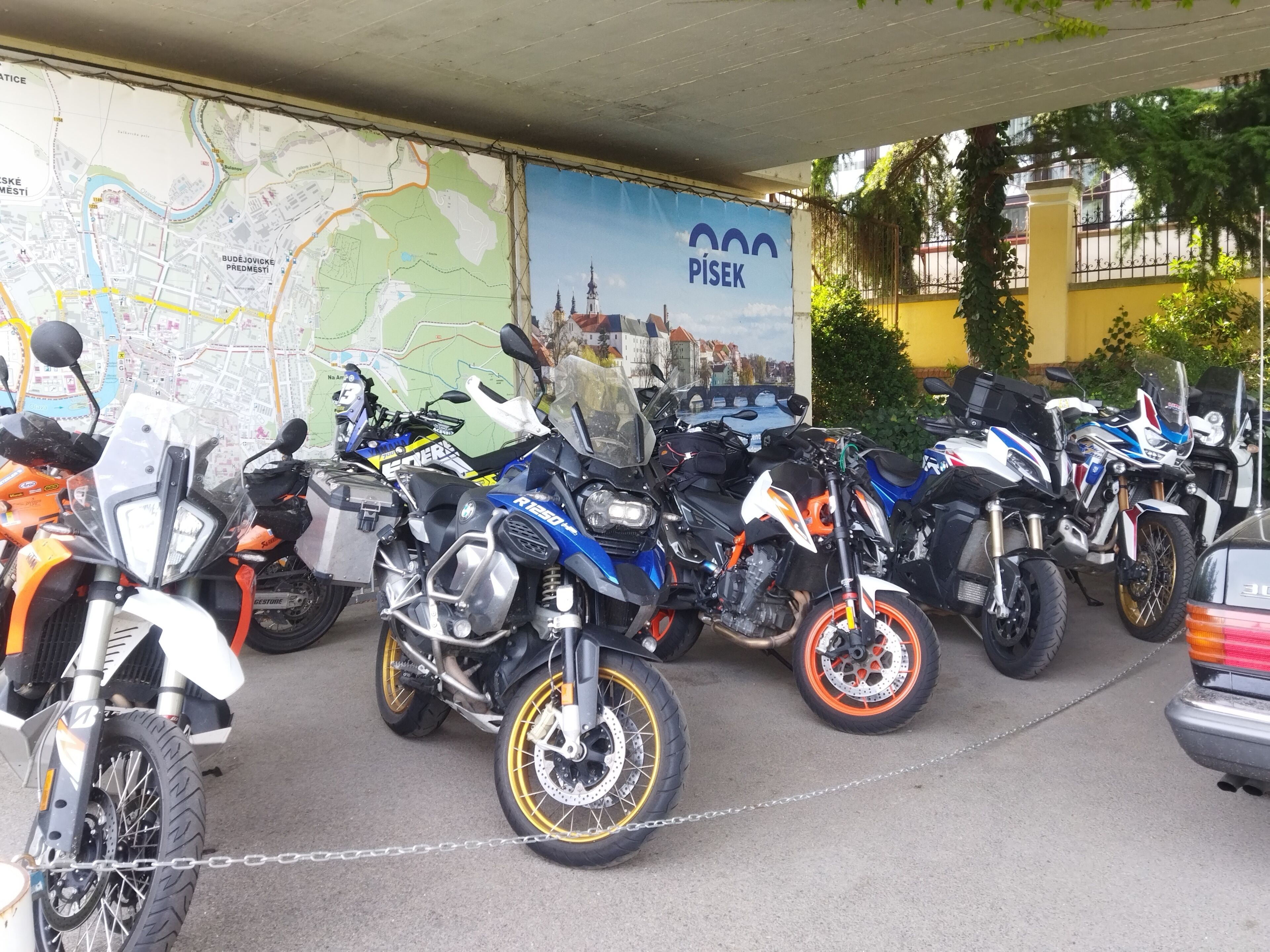 Motocicletas estacionadas em área coberta, com um mapa e uma placa ao fundo.
