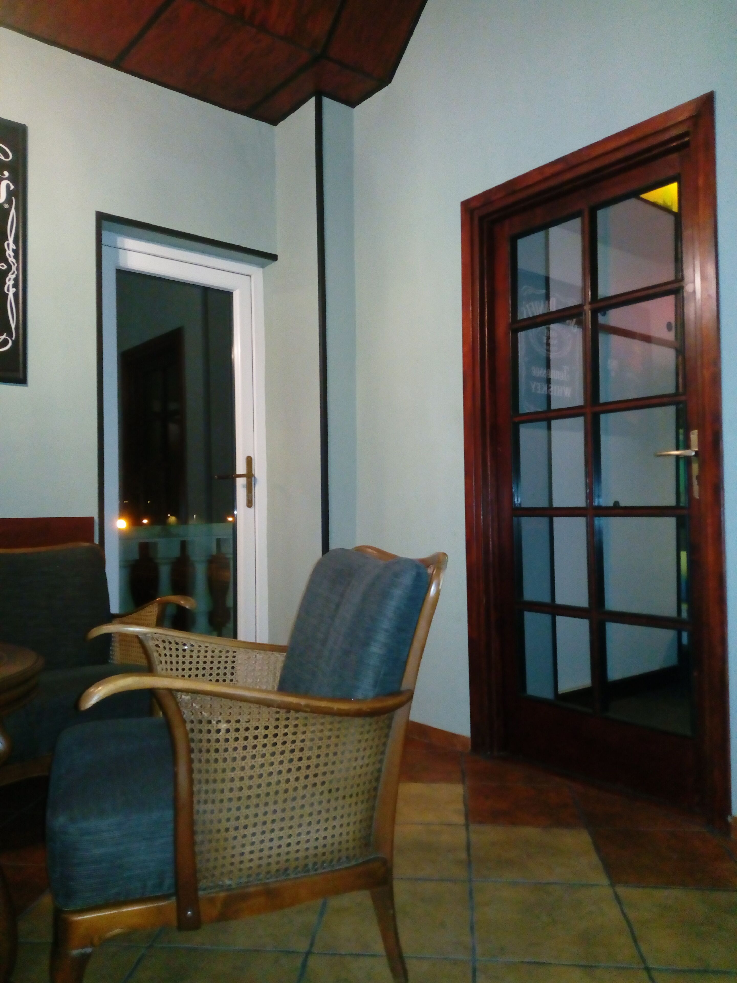 A room with a wooden door, a wicker chair, and a tiled floor.