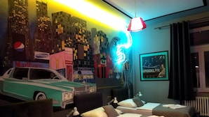 Quarto de hotel com duas camas, uma luz neon e um mural com vista para a cidade.