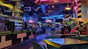 Uma área de bar com luzes neon, parede xadrez e uma motocicleta.