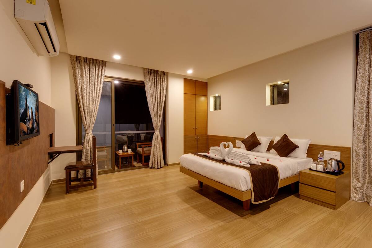 A hotel room with a large bed, a desk, a chair, a TV, and a window with curtains.