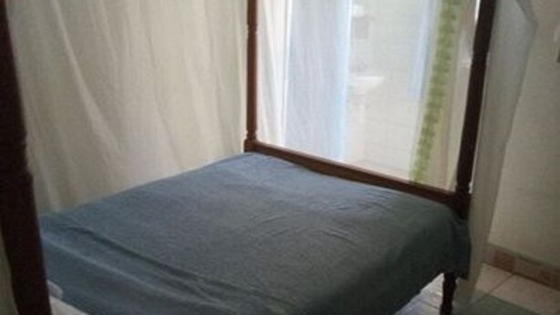 A single bed with a blue mattress and white sheets, a wooden frame, and a white canopy. - Lau Guest House (Machakos)