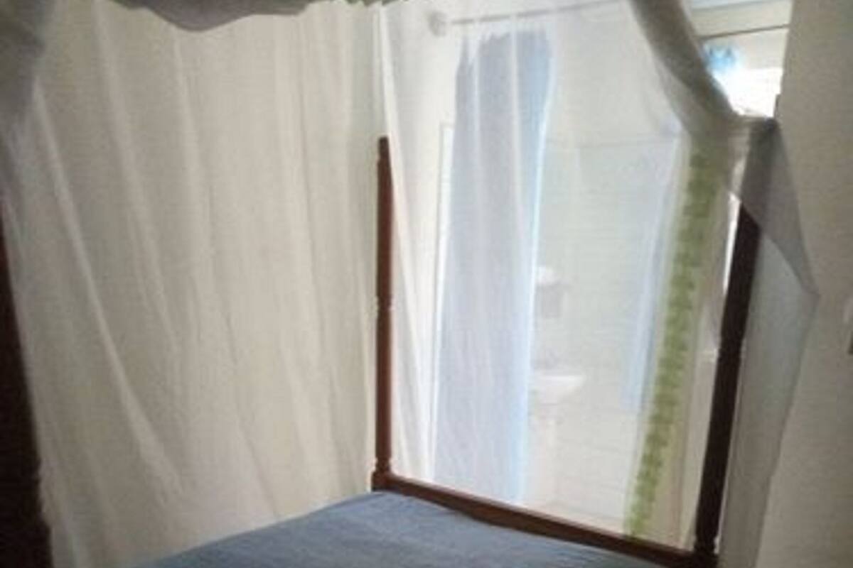 A single bed with a canopy, white curtains, and a tiled floor.