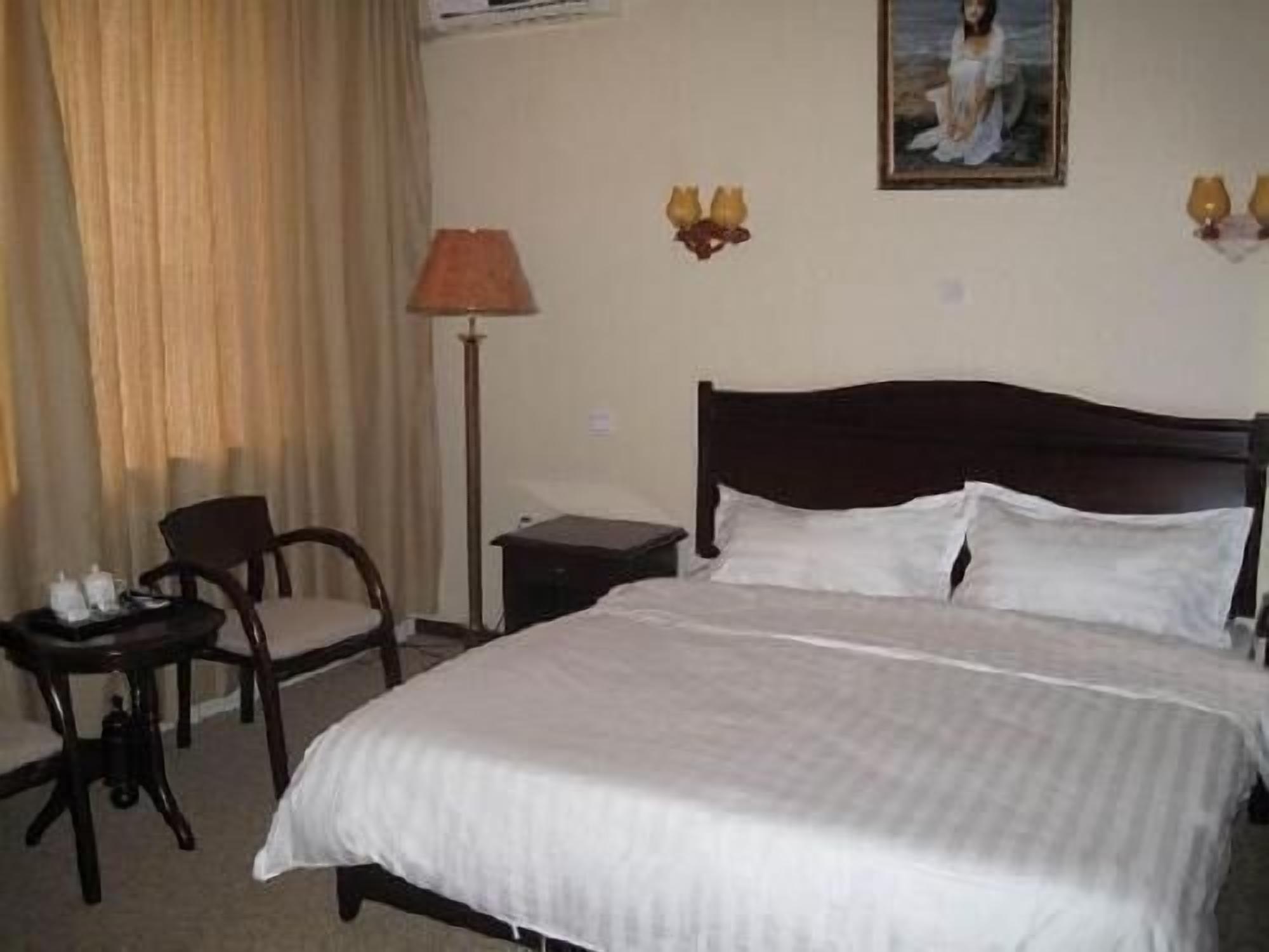 A neatly made bed with white linens, a wooden nightstand, a lamp, and a chair in a hotel room.