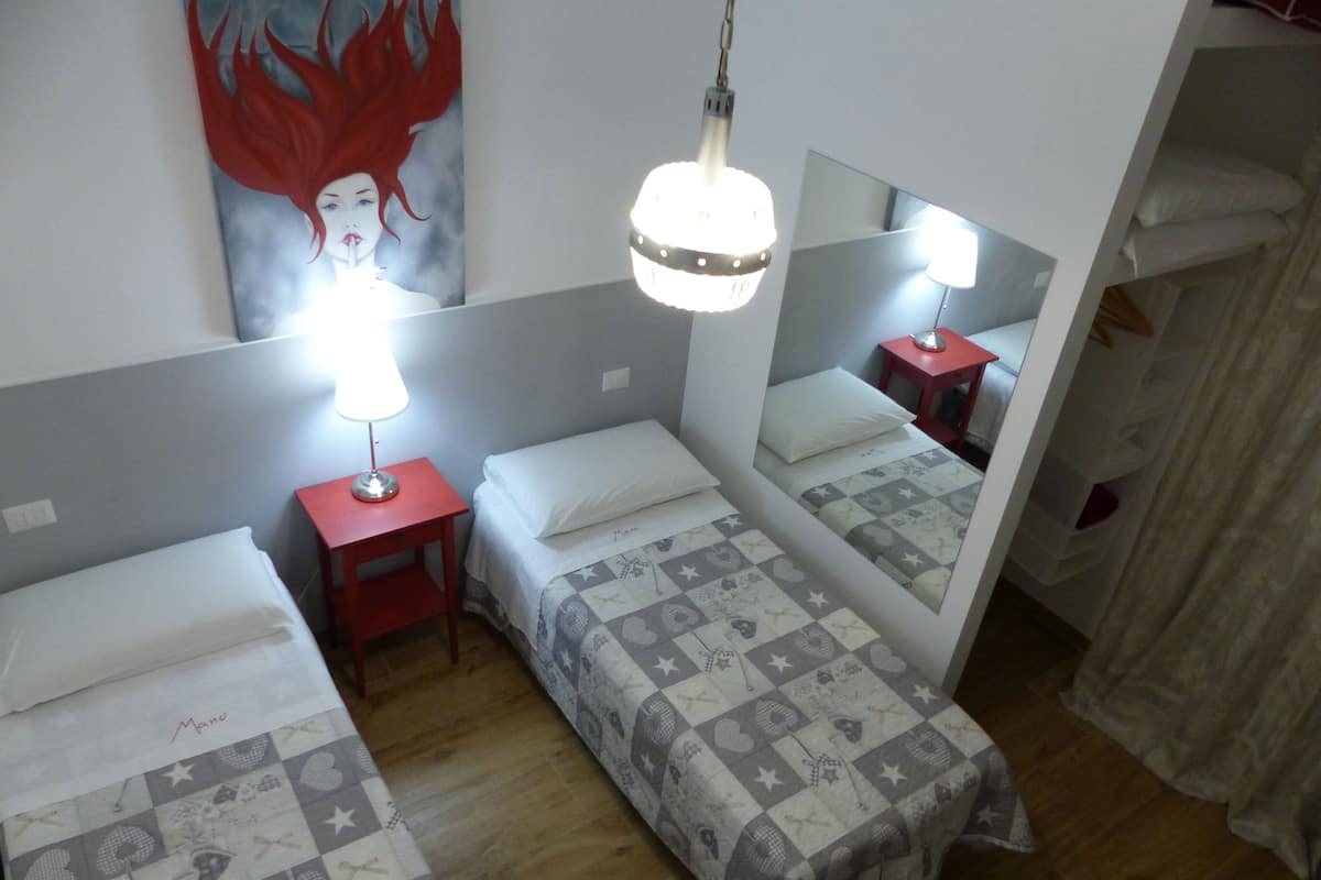 A room with two single beds, a red nightstand, a wall-mounted mirror, and a ceiling light fixture.