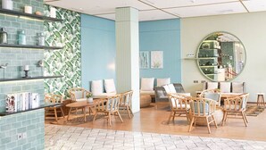 A modern lounge area with wicker furniture, a blue accent wall, and a tiled floor. - Louis Kienne Hotel Pemuda (Semarang)
