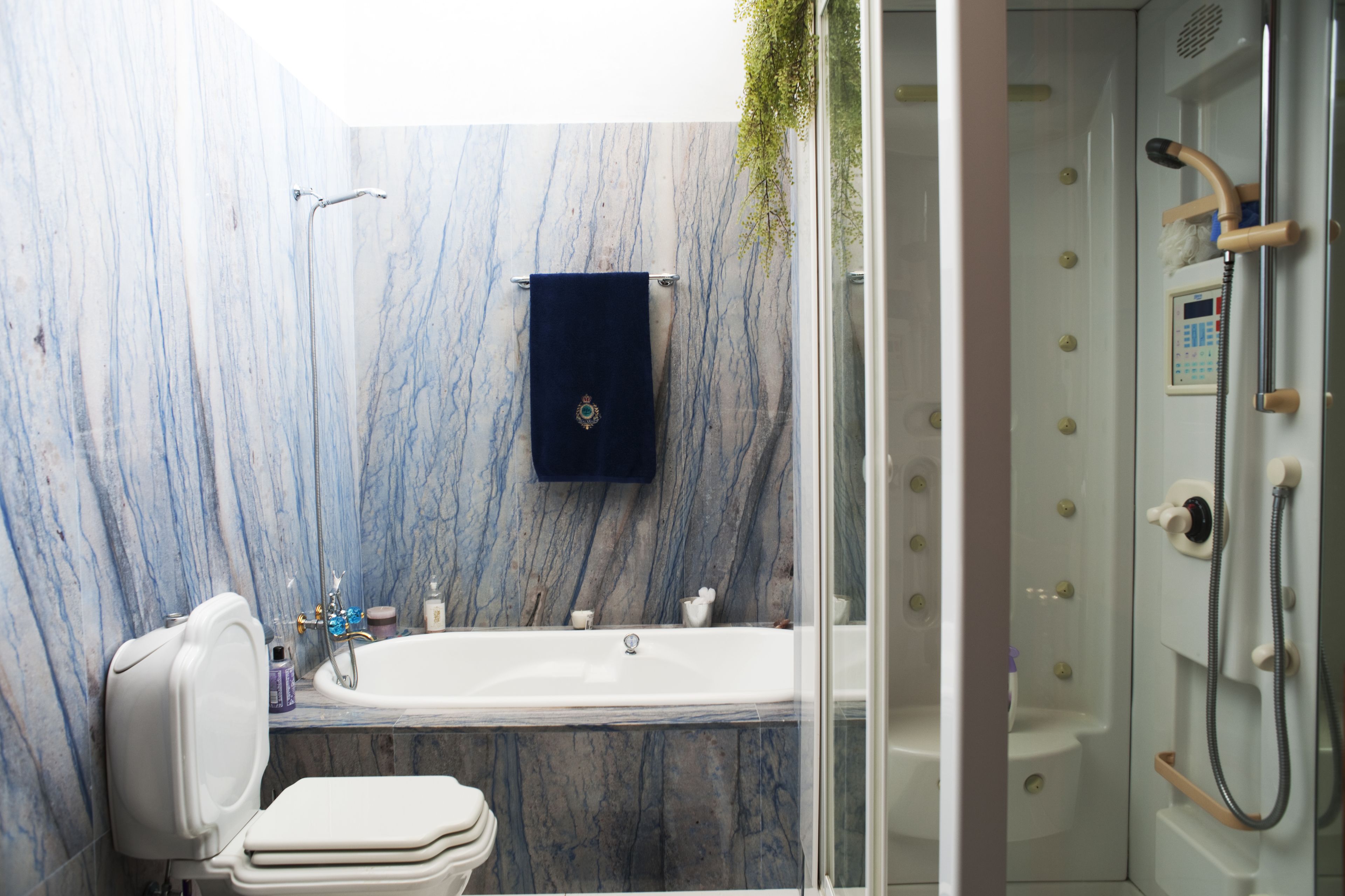 Un baño con pared de mármol, una bañera, un inodoro y zona de ducha con mampara de vidrio.