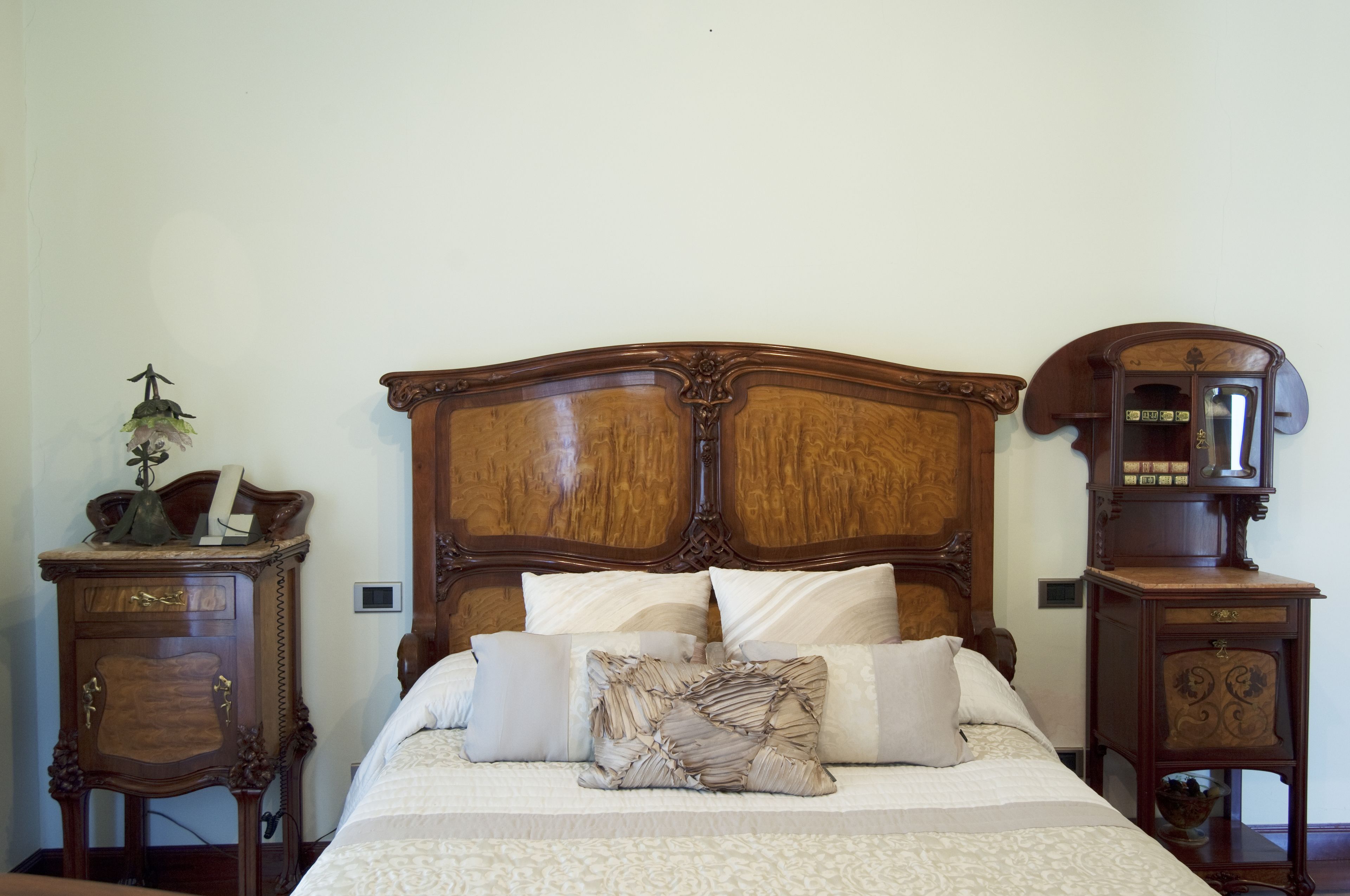 Een netjes opgemaakt bed met een houten hoofdbord, omringd door twee nachtkastjes met lades en een klein tafeltje met een lamp.