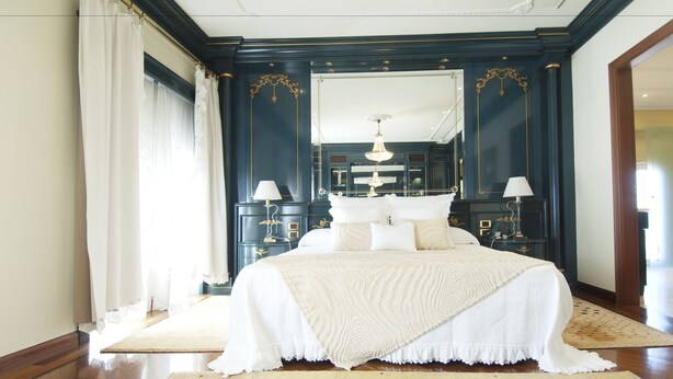 A bedroom with a large bed, two bedside tables with lamps, a mirror above the bed, and a wooden floor.