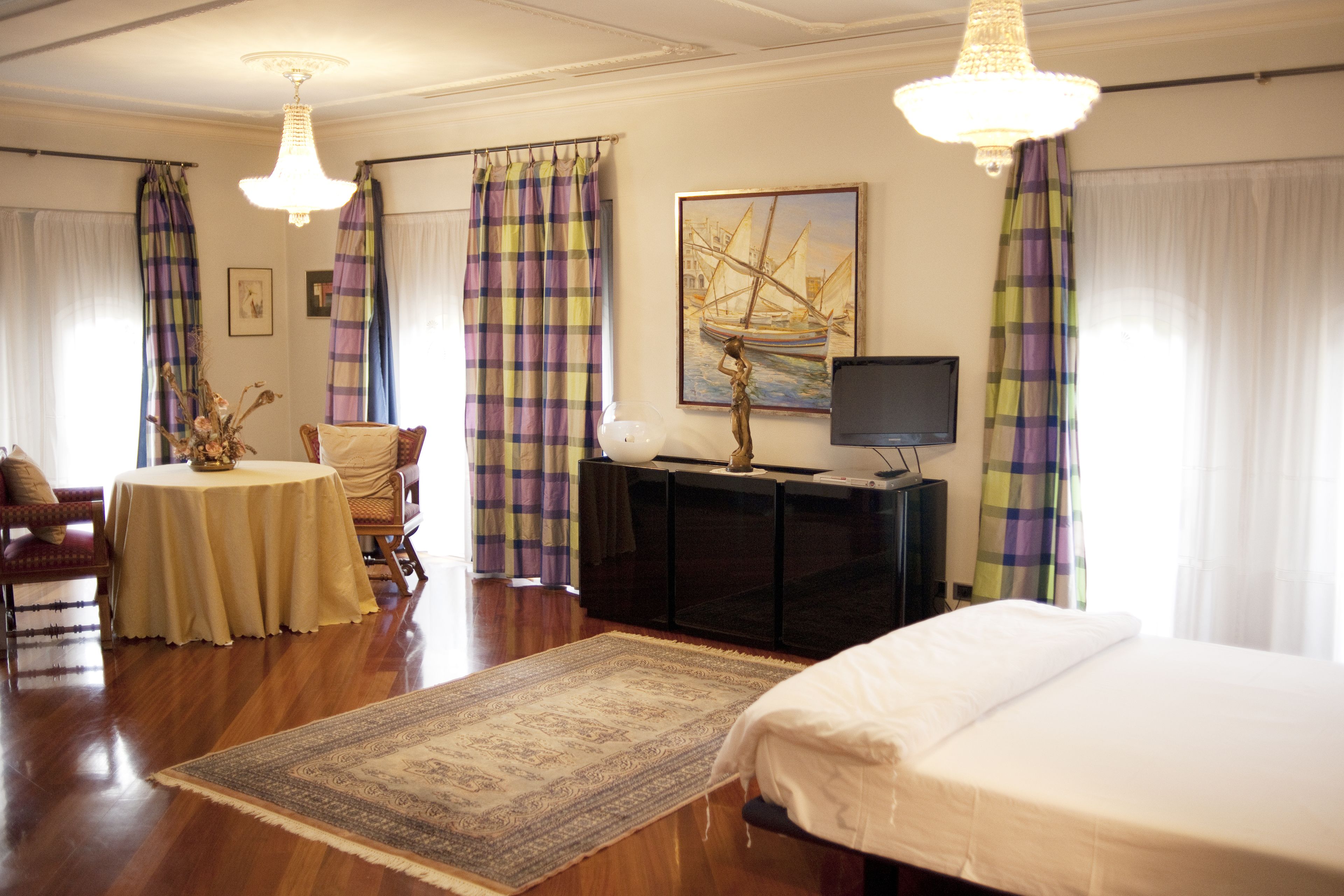 Een hotelkamer met een bed, een bureau met stoel, een televisietoestel, een schilderij en een kroonluchter.