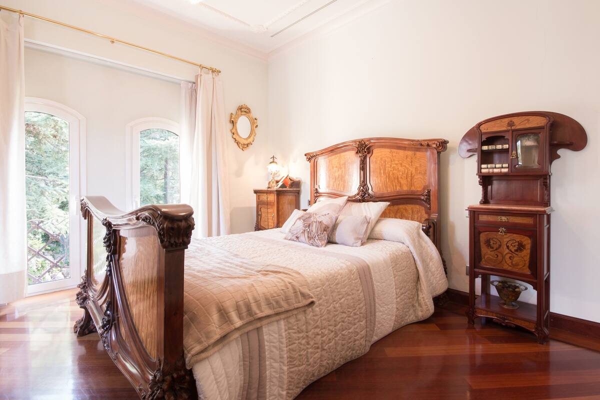 Une chambre à coucher classique, dotée d’un grand lit, de meubles en bois et offrant une vue sur la verdure environnante.
