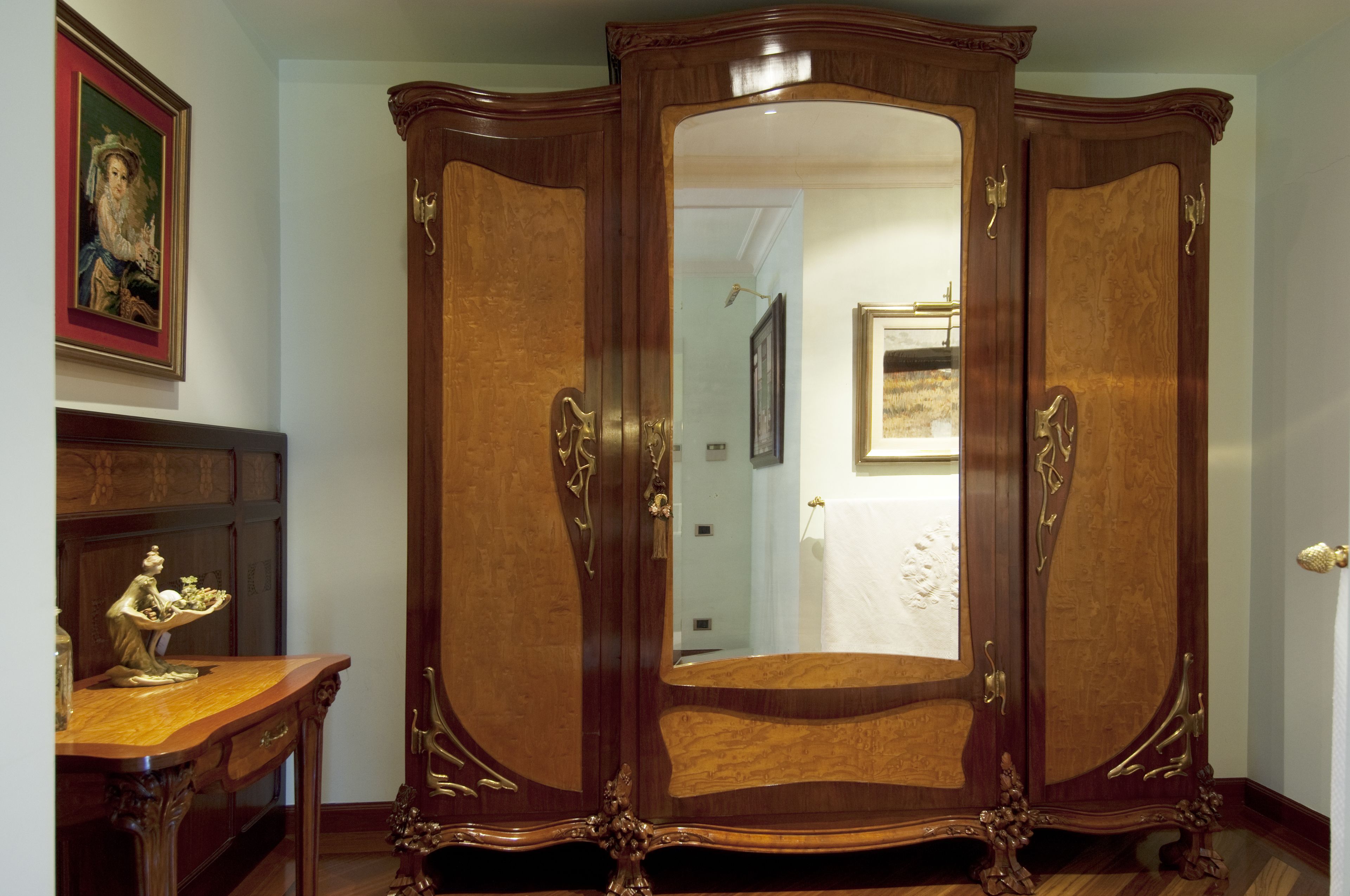 A room with a large wooden wardrobe, a small wooden table with a statue, and a framed painting on the wall.