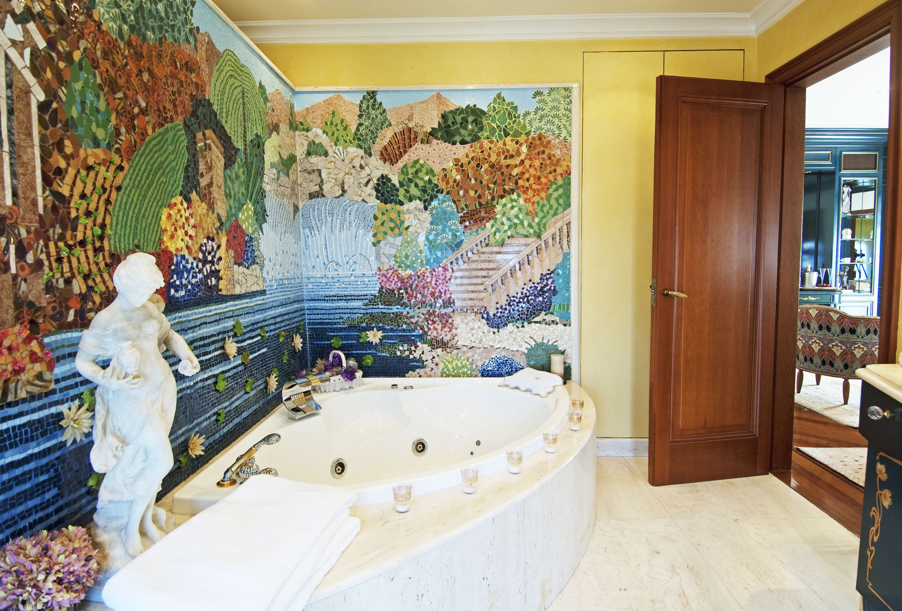 A bathroom with a mosaic wall, a large bathtub, and a statue.