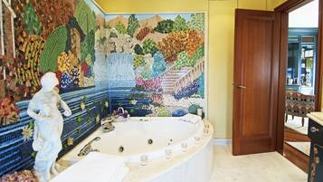 A bathroom with a mosaic wall, a large bathtub, and a statue.