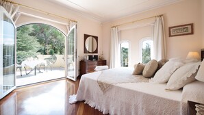 A spacious bedroom with a large bed, a dresser, and a balcony with a table and chairs.