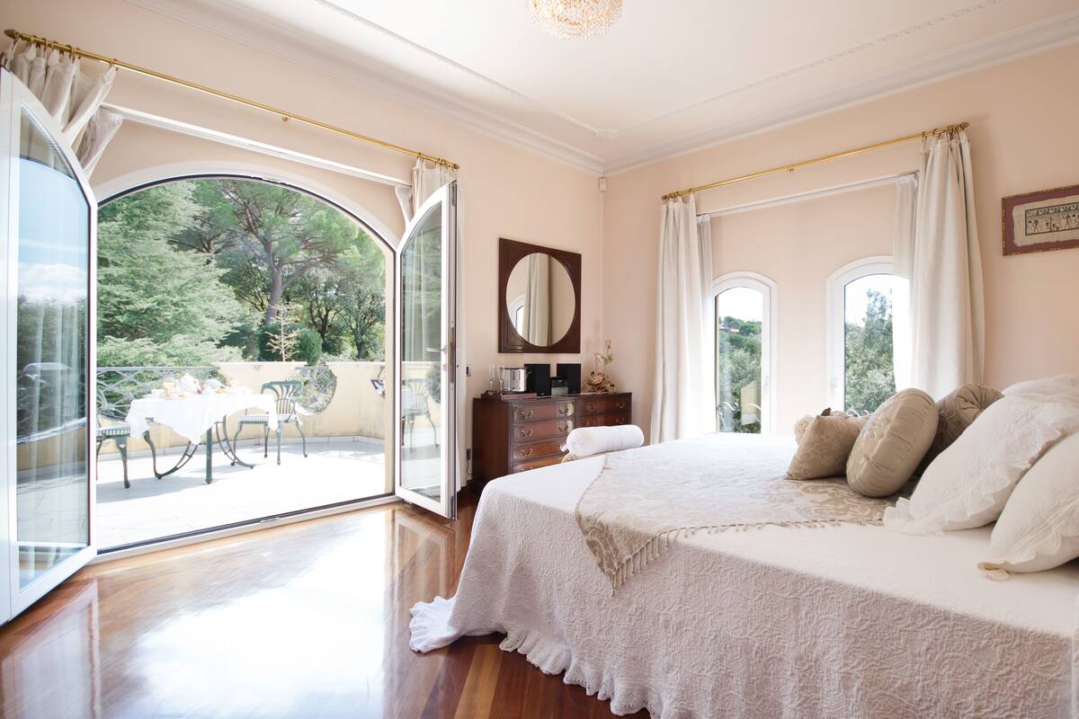 Une chambre spacieuse avec un grand lit, une commode et un balcon équipé d’une table et de chaises.